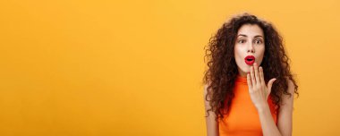 Şaşırmış ve heyecanlı beyaz bir kadının belden yukarı pozu. Kıvırcık saçlı, kırmızı rujlu, ağzı açık, onu avuç içi dinlemekten ağzı açık, şok edici dedikodular, şaşırtıcı haberlere şaşırıyor..