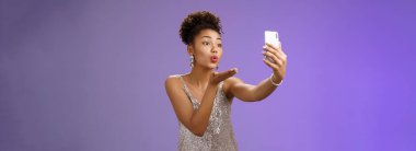 Zarif genç kız öğrenci mezuniyet balosunda eğleniyor video kayıttan keyif alıyor telefon ekranına bak hava öpücüğü gönder mwah yapıyor selfie Hold aleti alıyor, mavi arka planda duruyor..