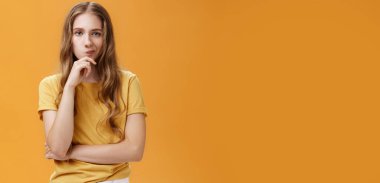 Hmm seçimler zordur. Ciddi görünümlü, yaratıcı genç bir kadının portresi. Dalgalı saçlı, çenesine gülümseyen, düşünceli bir şekilde el ele tutuşan, karar veren, turuncu arka plan üzerinde düşünen..