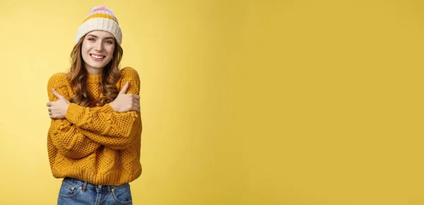 Getting cold bring jacket. Portrait charming tender feminine cute girlfriend embacing herself cuddling smiling warm gaze freezing outside standing knitted sweater hat, yellow background.