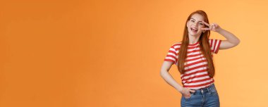 Dost canlısı, çekici, modern, kızıl saçlı üniversiteli kadın üniversite yıldızı, gözünün yanında barış işareti, mutlu bir şekilde gülümseme, pozitiflik, neşe ve güven, motivasyon kazanma, turuncu arka plan iyimser duruş..