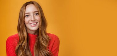 Turuncu arka plana karşı sevimli ve şehvetli pozlar veren, uzun doğal saç stili, neşeli bir şekilde gülümseyen yumuşak ve sevimli kızıl saçlı bir kızın yakın plan çekimi. Duygular