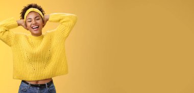 Kaygısız, neşeli, Afro-Amerikalı, süveter tokalı kız öğrenci. Ellerini başının arkasına koy. Rahatlatıcı bir poz ver..