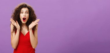 Heyecanlı ve hayret verici, zarif yetişkin pozu. Akşamları kırmızı rujlu kıvırcık saçlı kadın. Şaşkınlık içinde soluk soluğa kalan elbisesi. Avuçlarını sallayarak kameraya bakıyor..