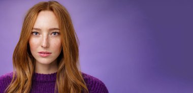 Şehvetli ve çekici kızıl saçlı, çilli, saf tenli, kameraya odaklanmış ve biraz açık ağızlı, mor arka planda poz veren bir kadın portresi. İnsanlar