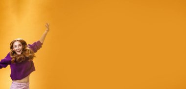 Mor kazaklı, neşeli, neşeli, neşeli, neşeli, neşeli ve neşeli bir kadın. Elleri havada, turuncu arka planda mutluluk ve neşe çığlıkları atarak zıplıyor. Anlaşıldı.