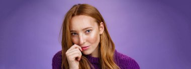 Kızıl kız şehvetli romantik bakışlarla büyülüyor. Kendine güvenen flört ve çekici kızıl saçlı kadının portresi. Başı dudaklara değiyor ve mor arka planda kameraya bakıyor..