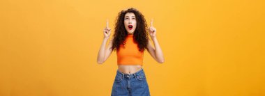 Şaşırmış duygusal ve karizmatik genç, kıvırcık saçlı, kırmızı rujlu bir kadının portresi turuncu arka planda etkilenmiş ve hayretler içinde kalmış. Boşluğu kopyala