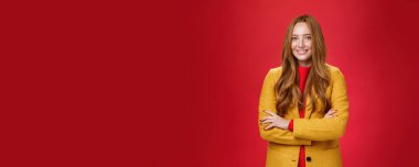 Yaşam tarzı. Sarı sonbahar ceketi içinde, kendinden emin bir şekilde el ele tutuşarak gülümseyerek mutlu ve mutlu bir şekilde kırmızı arka planda duran çekici ve başarılı genç bir bayan..