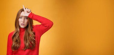 Kibirli ve kendini beğenmiş kızıl saçlı aşağılayıcı kadın alnında ezik işareti olan, alay eden ve küçümseyen rakip turuncu arka planda kendinden emin ve züppe duruyor. Boşluğu kopyala