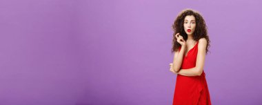 Kıvırcık saçlı, çekici, zarif bir bayan. Kırmızı elbiseli ve ruj katlayan dudaklı tuhaf bir şekilde saç teline dokunuyor ve mor üzerine yayılan dedikodulardan etkileniyor.