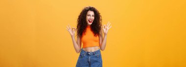 Cana yakın ve arkadaş canlısı beyaz bir kız. Kıvırcık saçlı, kısa şortlu. Onaylı jest yapıyor. Turuncu duvarın üstünde kameraya gülümseyen muhteşem partileri sevdiğini söylüyor..