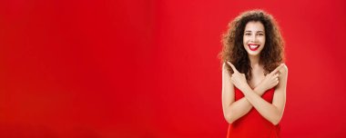 Seçimlerden memnun olan bir kadın zarif kırmızı bir gece elbisesi içinde göğsünde sol ve sağ elini gösteren kıvırcık saç stili ile mutlu mesut ayakta duruyor. Anlaşıldı.