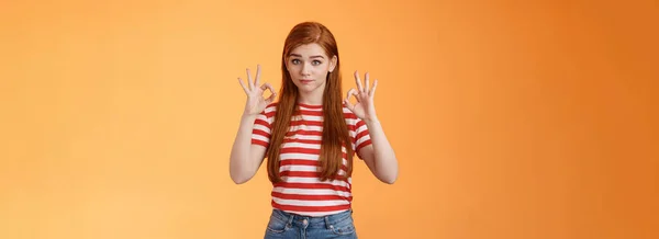 Not bad, but okay. Silly tired redhead woman show approval ok sign, pouting raise eyebrows, feel exhausted after finishing job, show excellent, good work gesture, stand orange background.