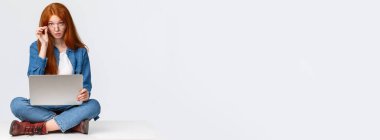 Müsaadenizle, meşgulüm. Sorgulanan kızıl saçlı kız öğrenci proje hazırlıkları sırasında durduruldu, internette ders için malzeme aranıyor, yerde dizüstü bilgisayarla oturan meraklı kameraya bakın.