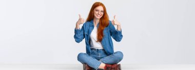 Mükemmel, tatmin ve insan konsepti. Sevimli, destekleyici, kızıl saçlı kız arkadaş yerde oturuyor, bacaklarını kavuşturmuş, gülümsüyor ve tezahürat yapıyor..