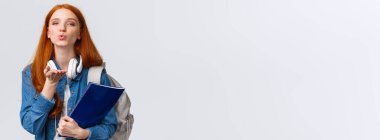 Sevimli ve hassas, şehvetli bir üniversiteli kız, kızıl saçlı şımarık bir öğrenci, hava öpücüğü gönder, kameraya tutkuyla üfle, sırt çantası ve klasörü tut..