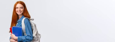 Salonda sınıf arkadaşını gören bir kız, selam vermek için geri dönüyor, sevinçle gülümsüyor, sırt çantası ve defterler tutuyor, sınıfa geri dönüyor, üniversitede okuyor, beyaz arka planda duruyor..