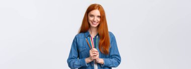 Hayatı canlandırma zamanı. Cazibeli, kendine güvenen, kot gömlekli, kameraya gülümseyen, elinde renkli kalemler olan, beyaz arka plan çizimi yapan çekici, karizmatik kız derslere katılıyor..