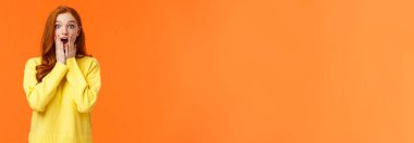 Etkilenmiş ve nutku tutulmuş kızıl saçlı kadın müthiş bir haber aldı, nefes nefese kaldı, ağzı açık kaldı hayrete düştü, yanaklarına dokundu ve kameraya baktı, yılbaşı alışveriş sezonu başladı, turuncu arka plan.