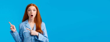 Şaşırmış kızıl saçlı kız özel bir teklif buldu. İndirim tanıtımı, sağ üst köşeyi gösterme, gece kıyafeti giyme, pijama partisi hakkında dedikodu yapma, mavi arka plan. Boşluğu kopyala