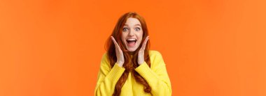 Heyecan, duygular ve tatil konsepti. Belden yukarısına ateş eden neşeli ve heyecanlı kızıl saçlı kadın heyecan ve sevinçten çığlık atıyor, elele tutuşuyor, ağzını açıyor ve hayrete düşüyor..