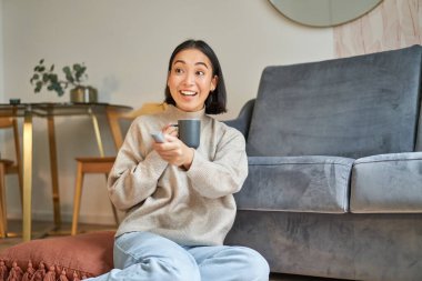 Gülümseyen genç bir kadının portresi. Televizyon seyrediyor, yerde oturuyor ve fincandan kahve içiyor..