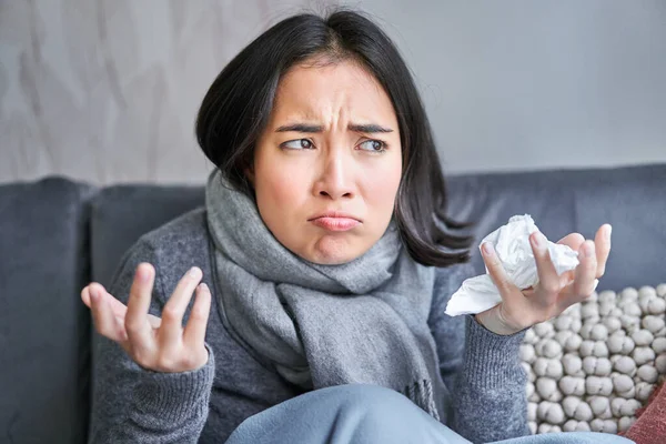 Cost of living and heating problems. Close up of angry girl sneezing, staying at home and freezing, wearing warm clothes and scarf.