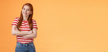 Neşeli, sevimli, kızıl saçlı, 20 'li yaşlarda, çapraz kollu, geniş gülümseyen, neşeli konuşan arkadaş, sırıtan, turuncu arka planda duran, keyifli, iyi hisseden, rahat bir kot giyen.