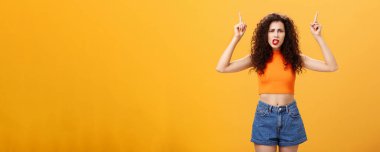 Kıvırcık saç stili olan hoşnutsuz bayan müşterinin kapalı çekimleri. kırmızı ruj serinletilmiş üst kısmı, kafa karıştırıcı ve tatminsiz bir ifadeyle portakal rengi üzerinden açıklama talep ediyor.