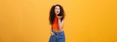 Şık, cilveli, kendine güvenen, kıvırcık saçlı, kırmızı rujlu, kameraya karşı şehvetli bir şekilde gülümseyen bir kadın.