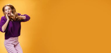 Yaşam tarzı. Etkilenmiş ve şaşırmış, mor kazaklı güzel saçlı kadın ağzı açık ve yanaklarında el ele tutuşmuş turuncu arka planda eğlenen zıplayan gözler gibi..