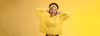 Kaygısız genç, çekici, Afro-Amerikalı. Kız ellerini başının arkasına koyup dinleniyor tembellik ediyor boş günlerin tadını çıkarıyor gülümsüyor ve boş zamanlarını sarı arka planda eğlenerek geçiriyor..