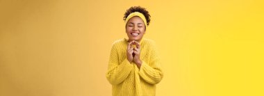 Çekici, iyimser, gamsız, gülümseyen Afro-Amerikan kadın. Gözlerini kapat dua et mutlu bir şekilde avuçlarını birleştir dileğin gerçekleşsin şanslı gününde neşeli sarı arka planda dur.