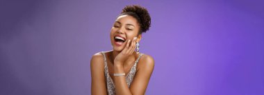 Neşeli, çekici, mutlu, Afro-Amerikalı, zarif, gümüş renkli, hafif elbiseli, gülüyor, gülüyor, eğleniyor, erkek arkadaşından zevk alıyor, espriler yapıyor, cilveli bakışlar atıyor, mavi arka plan..