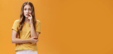 Endişelenen kız yeni dövmeye tepki veriyor. Endişeli ve gergin, aptal, kendine güveni olmayan, doğal saç stili ısıran, panikleyen, endişeli ve turuncu duvarın üzerinden sorunlu görünen genç bir kadının portresi.