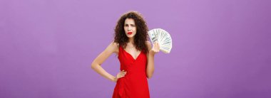 Kadın kocasının zulasını sorgulanıyor ve kafası karışmış halde bulmuş. Kırmızı elbiseli, kıvırcık saçlı, düşünceli, çekici ve zarif karısı mor arka planda bir sürü para sallıyor..