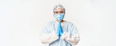 Lütfen aşılayın. Kişisel koruyucu ekipman içinde gülümseyen Asyalı kadın doktor ya da hemşire, yalvarma, rica etme hareketi, beyaz arka planda dikilme.