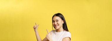 Covid-19 aşı konsepti. Sevimli aşılı Asyalı kadın reklam metni için boş yerleri işaret ediyor, sarı arka plan..