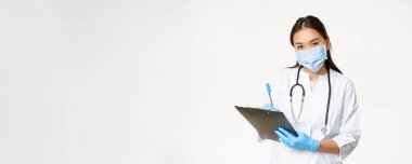 Maskeli ve eldivenli gülümseyen Asyalı kadın doktor, hasta teşhisi, reçete, elinde kalem ve dosya, beyaz arka plan..
