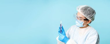 Test tüpünde kimyasalları karıştıran laboratuvar çalışanı, koruyucu ekipman ve güvenlik gözlüğü takıyor, mavi arka plan..