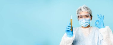 Laboratuvar çalışanı, kişisel koruyucu ekipman hemşiresi, test tüpünde numune gösteriyor ve tamam işareti, test hastası analizi, mavi arka plan..