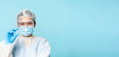 Asyalı kadın doktor portresi yakın çekim, kişisel koruyucu ekipman hemşiresi aşıyı gösteren şırınga, grip aşısı ya da mavi arka plan.