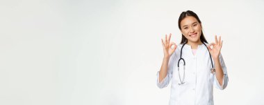 Gülümseyen kadın doktor, sağlık kliniği üniformalı Asyalı sağlık görevlisi iyi belirtiler gösteriyor, onay veriyor, hasta izni veriyor, beyaz arka planda duruyor..