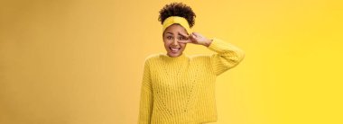 Aptal, kendine güveni olmayan, utangaç, genç ve utangaç bir kız. Yüzü kızaran, gülümseyen, barış zaferi işareti olan, poz veren, dost canlısı sarı arka plan. Boşluğu kopyala