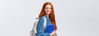 Salonda sınıf arkadaşını gören bir kız, selam vermek için geri dönüyor, sevinçle gülümsüyor, sırt çantası ve defterler tutuyor, sınıfa geri dönüyor, üniversitede okuyor, beyaz arka planda duruyor..