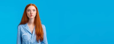 Balık gibi sessiz. Sevimli ve komik kızıl saçlı, uzun kızıl saçlı, dudaklarını taklit ederek emen, neşeli bir şekilde oynaşan, gece elbisesi giyen, mavi arka planda duran,.