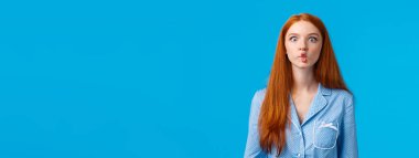 Balık gibi sessiz. Sevimli ve komik kızıl saçlı, uzun kızıl saçlı, dudaklarını taklit ederek emen, neşeli bir şekilde oynaşan, gece elbisesi giyen, mavi arka planda duran,.