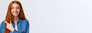 Heyecanlı ve etkilenmiş, heyecanlı, heyecanlı kızıl saçlı, uzun saçlı, kızıl saçlı, mavi gözlü, neşeli kameraya bakan, merak içinde sırıtan, sol parmağı işaret eden, harika bir haber buldu..