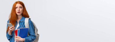 Hüzünlü ve hüzünlü, tatlı, kızıl saçlı, sorunlu görünen bir kadın, akıllı telefon ekranında endişe verici bir şey okuyor, cep telefonu, sırt çantası ve defterleri tutuyor, üniversitedeki gibi..